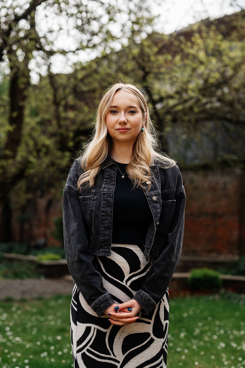 A female student in patterned skirt stands under a beautiful tree in Wilberforce House gardens