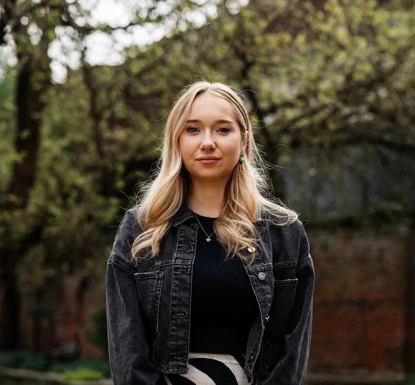 A female student in patterned skirt stands under a beautiful tree in Wilberforce House gardens