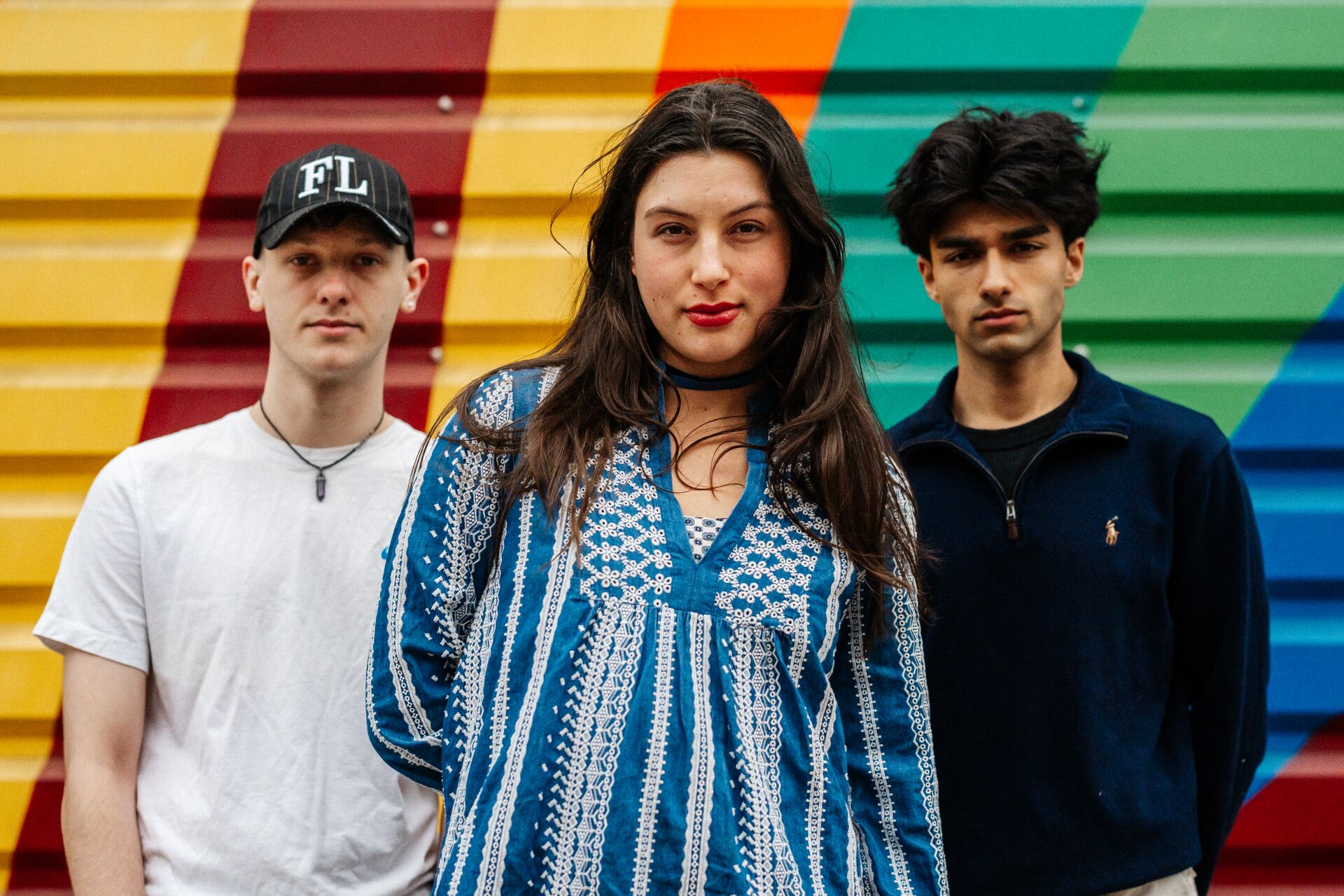 Three of Hull’s students stand confidently together in front of a bright mural painted on shutters