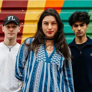 Three of Hull’s students stand confidently together in front of a bright mural painted on shutters