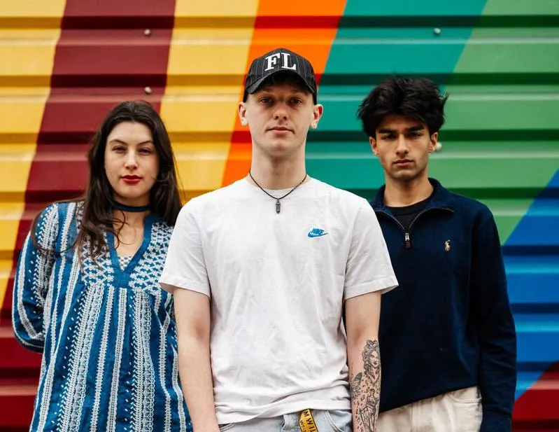 Three of Hull’s students stand confidently together in front of a bright mural painted on shutters