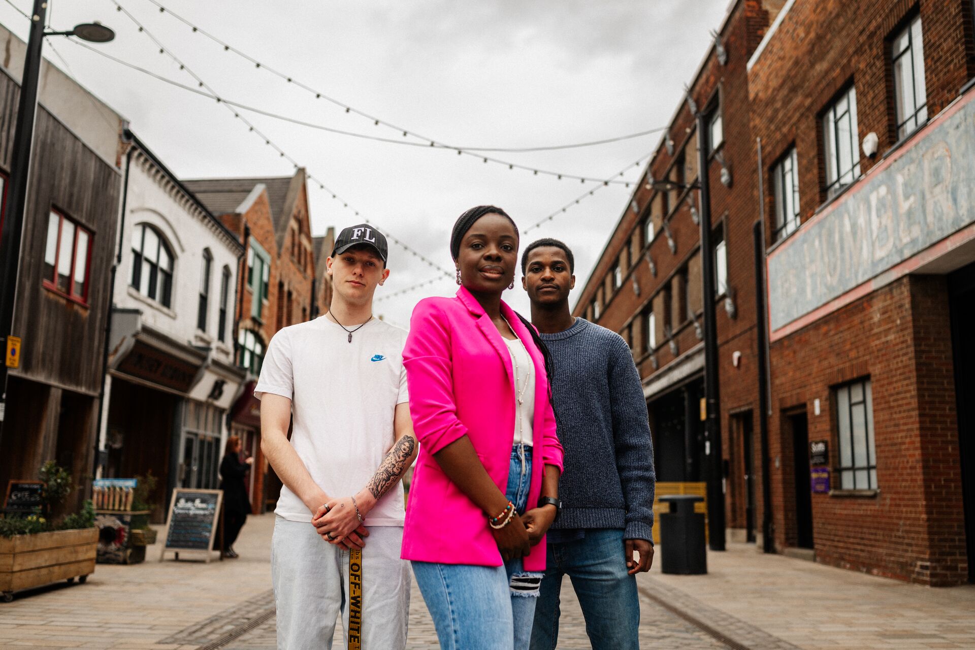 Three of Hull’s students stand confidently together under string lights on Humber Street