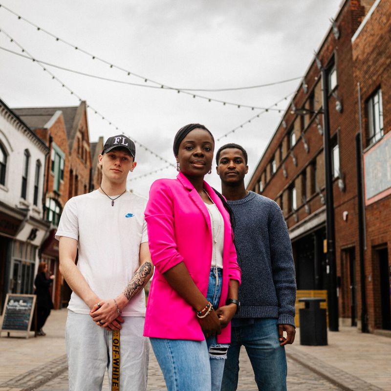 Three of Hull’s students stand confidently together under string lights on Humber Street