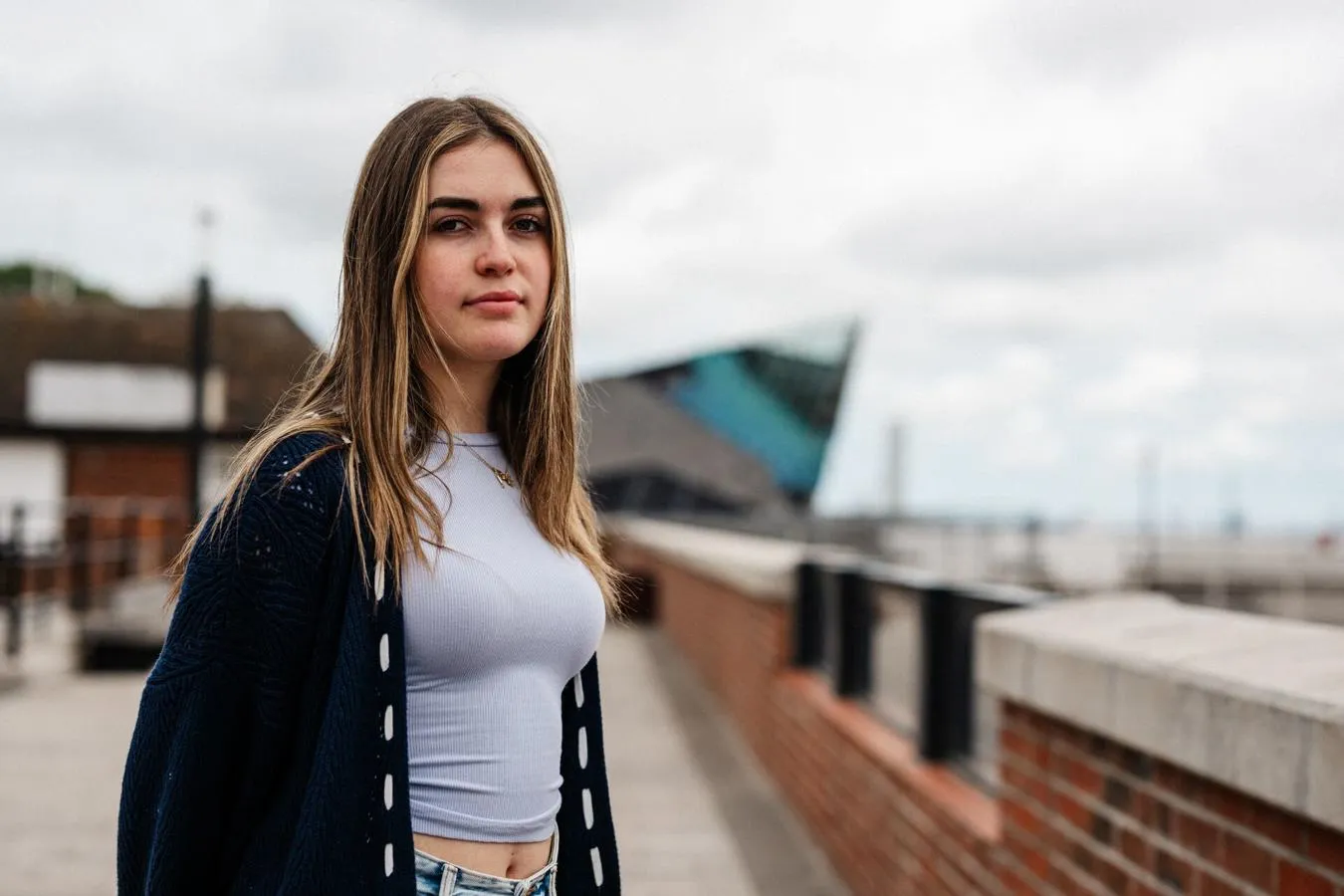 A female student in grey top stands confidently in front of The Deep, Hull's iconic aquarium