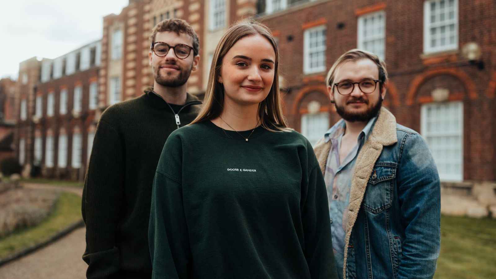 Three students posing outside a red brick building