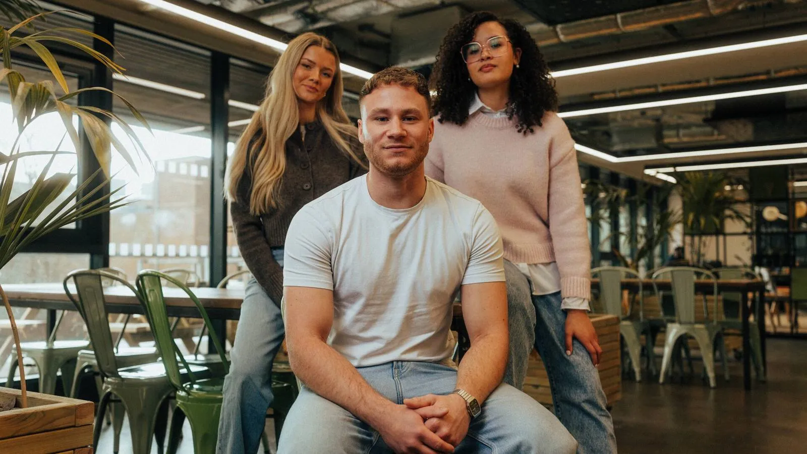 Three students posing in front of a room full of plants