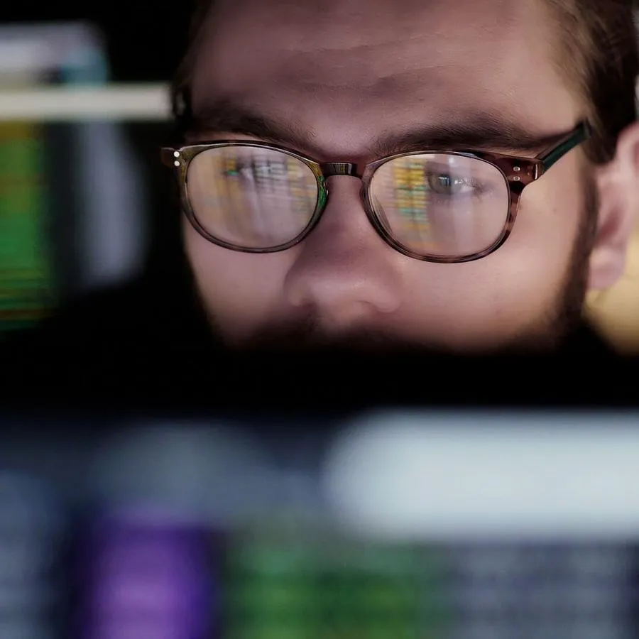 Man with glasses looks intently at a computer screen