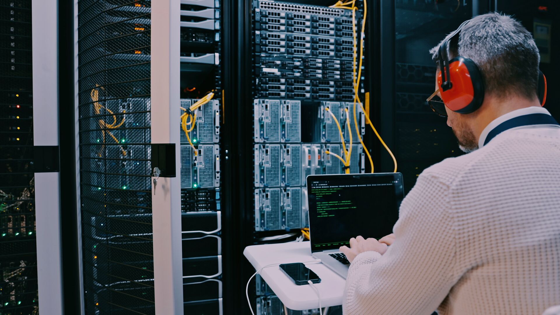 ICT technician wearing headphones running diagnostics on a laptop in front of a large server