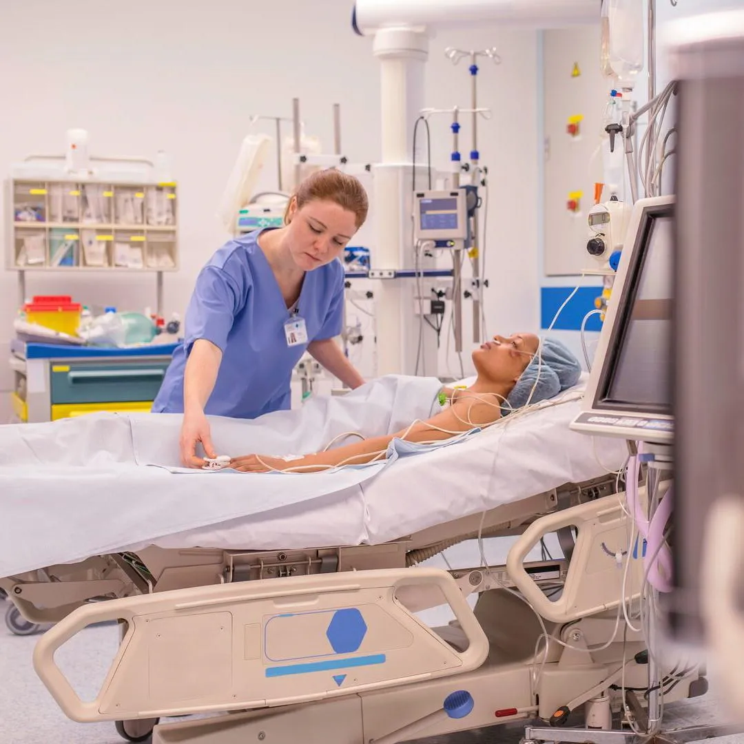 A nurse in a blue uniform practising on a mannequin laying on a hospital bed