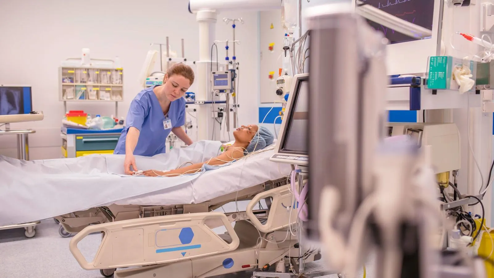 A nurse in a blue uniform practising on a mannequin laying on a hospital bed