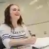 A student smiles whilst writing on paper.