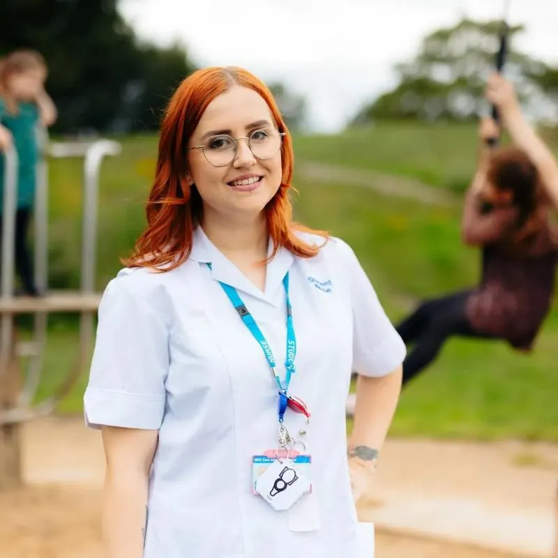 A student nurse with three children playing on equipment in a park