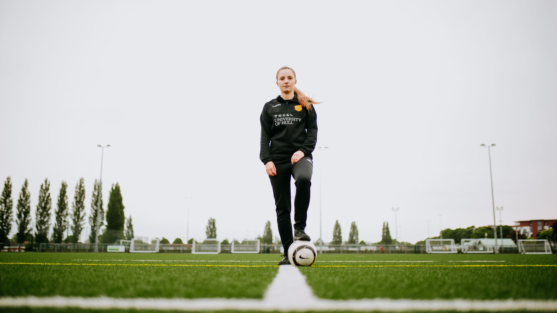 A student stood in the middle of a football field with their foot on the ball