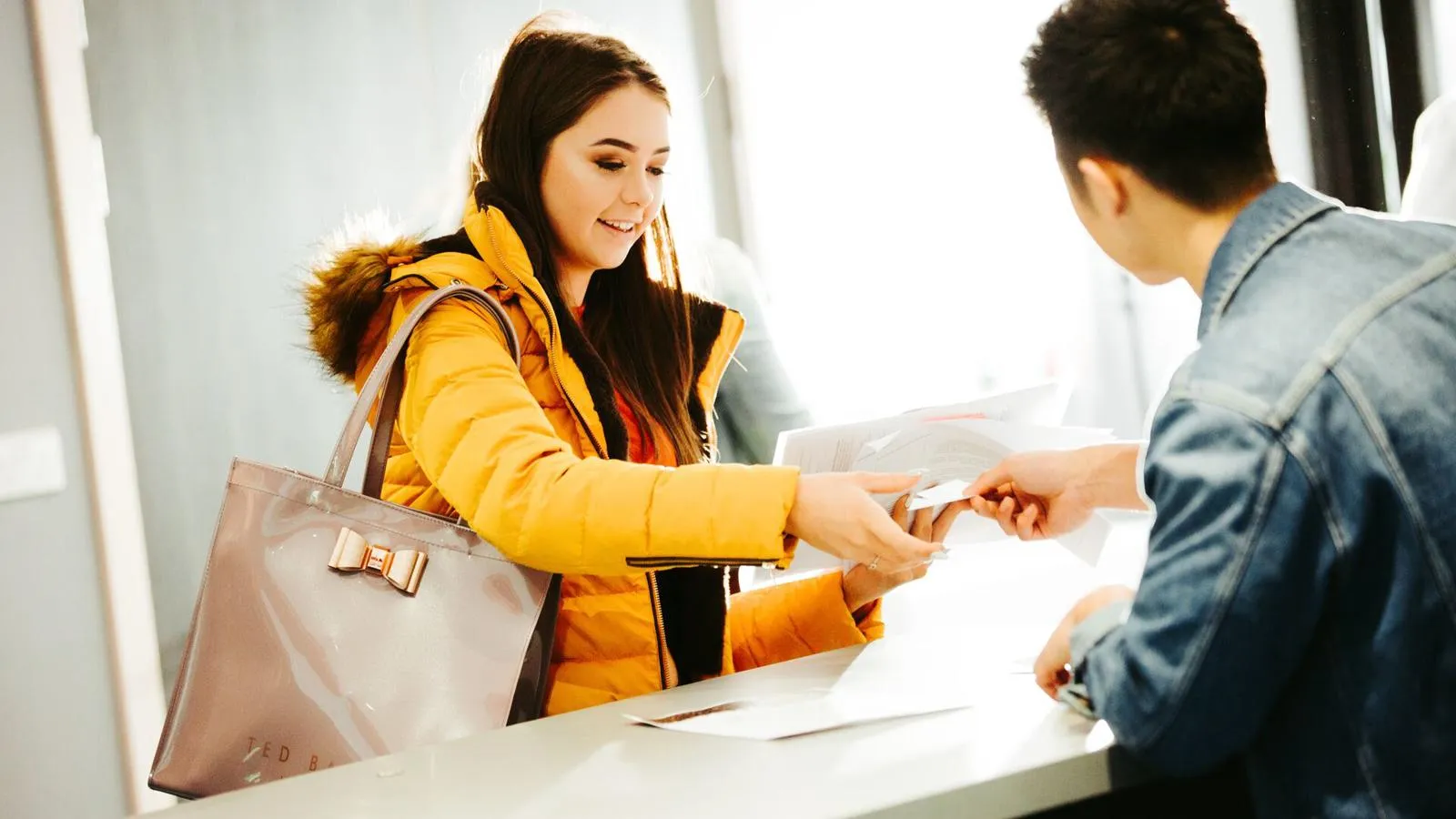Student handing files across desk to reception, moving in to accommodation