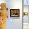 A sculpture in the library art gallery with paintings on the wall in the background