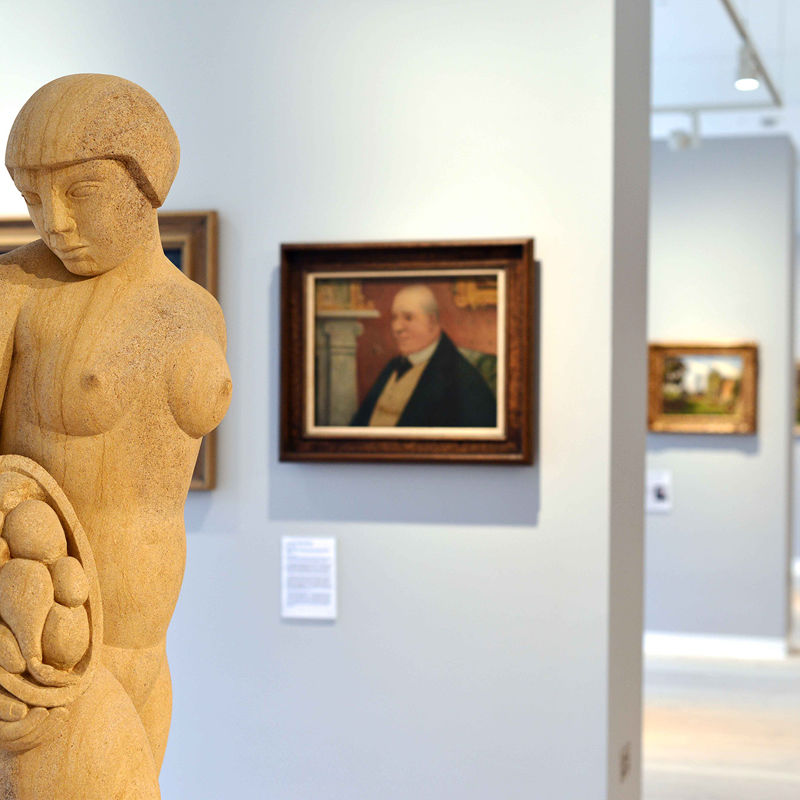 A sculpture in the library art gallery with paintings on the wall in the background