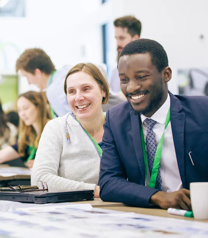 Three smiling people around a table at a conference with more in the background