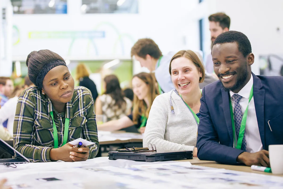 Three smiling people around a table at a conference with more in the background