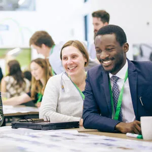 Three smiling people around a table at a conference with more in the background