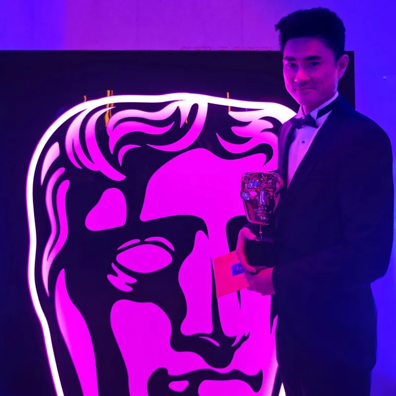 Alumni stood holding a BAFTA.
