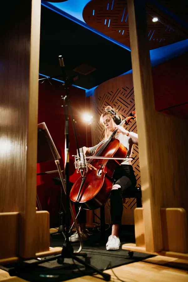 A female student plays a cello in a recording studio booth