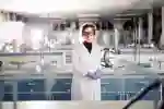 Student in lab coat stood confidently in a large laboratory.