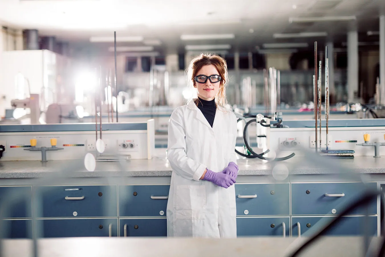 Student in lab coat standing confidently in a large laboratory.