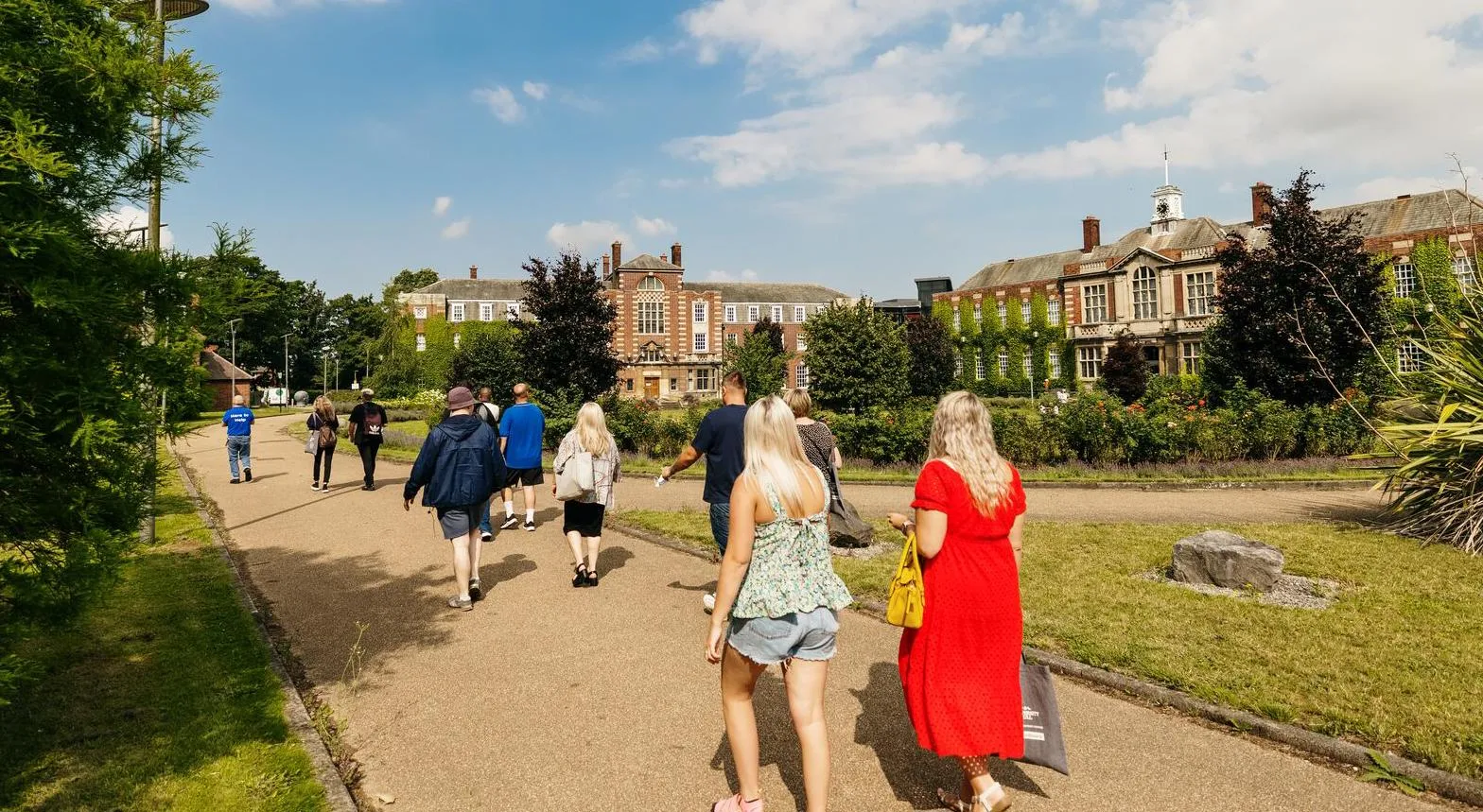 People walking on paths between lawns outside grand University of Hull building.