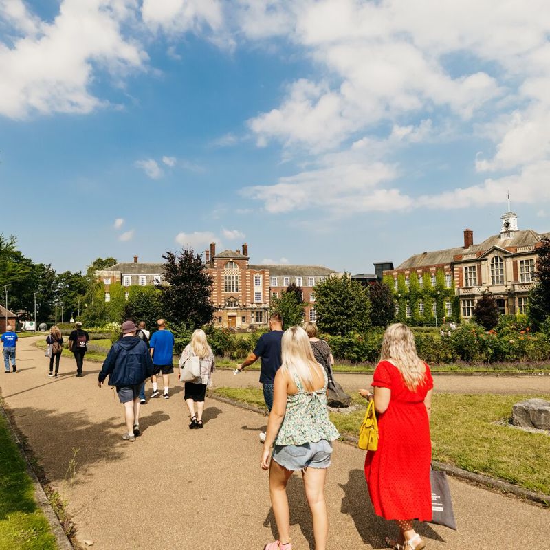 a group of potential students walking in front of old style university buildings on a sunny day