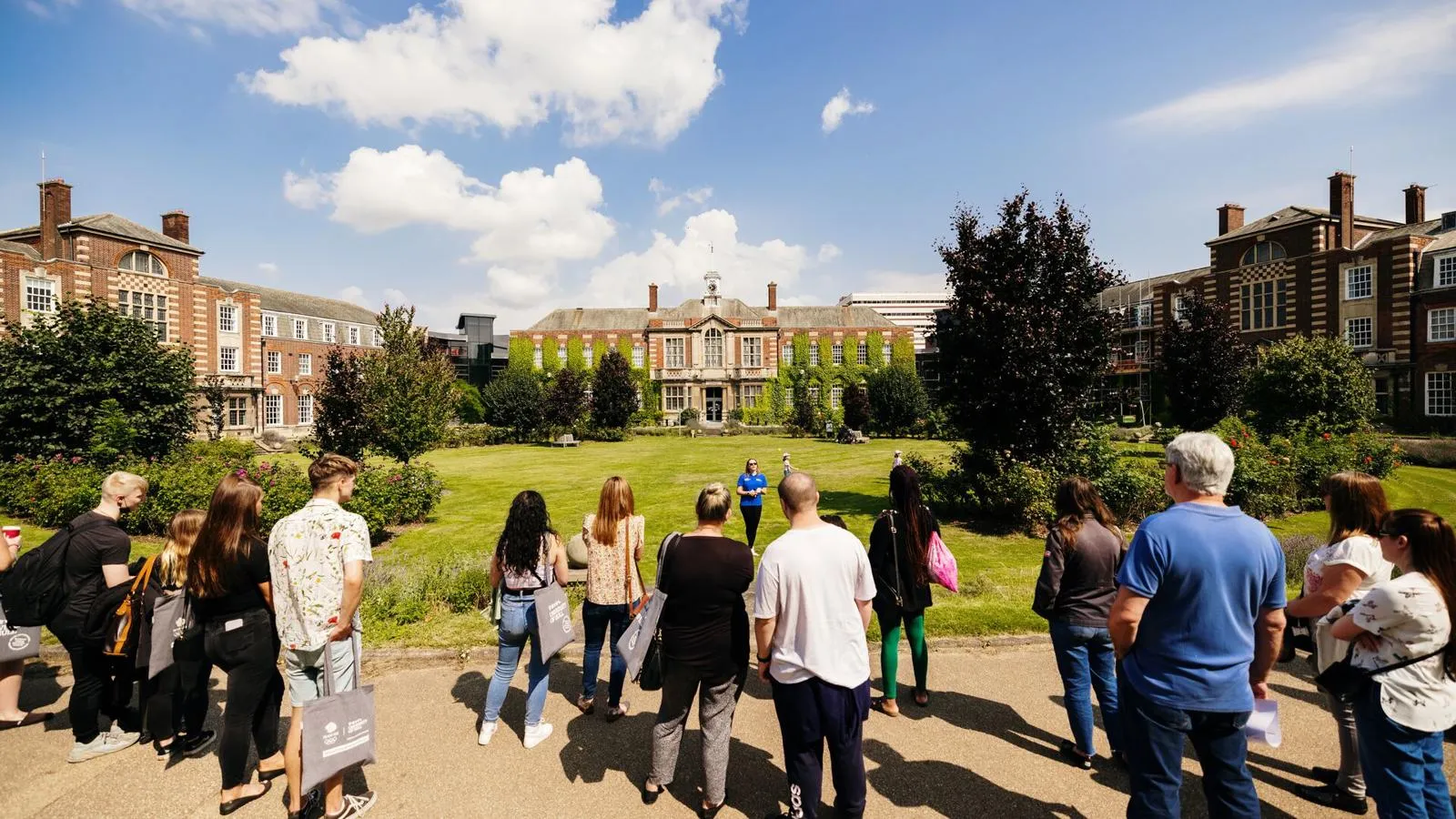 crowd gathered in front old an old style university building and student ambassador giving a tour