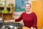 MA Education academic Cathy sits smiling in a teaching classroom with plastic animals on a table in front of her.