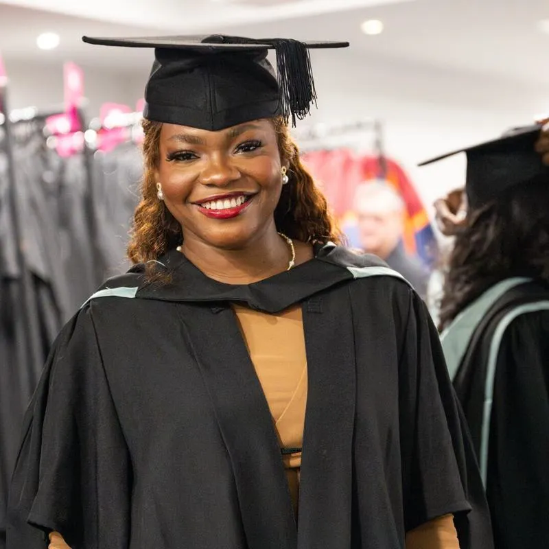 Female student smiling at camera in a cap and gown celebrating graduation
