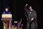 Graduating student rasing hand to crowd whilst collecting certificte