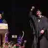 Graduating student rasing hand to crowd whilst collecting certificte