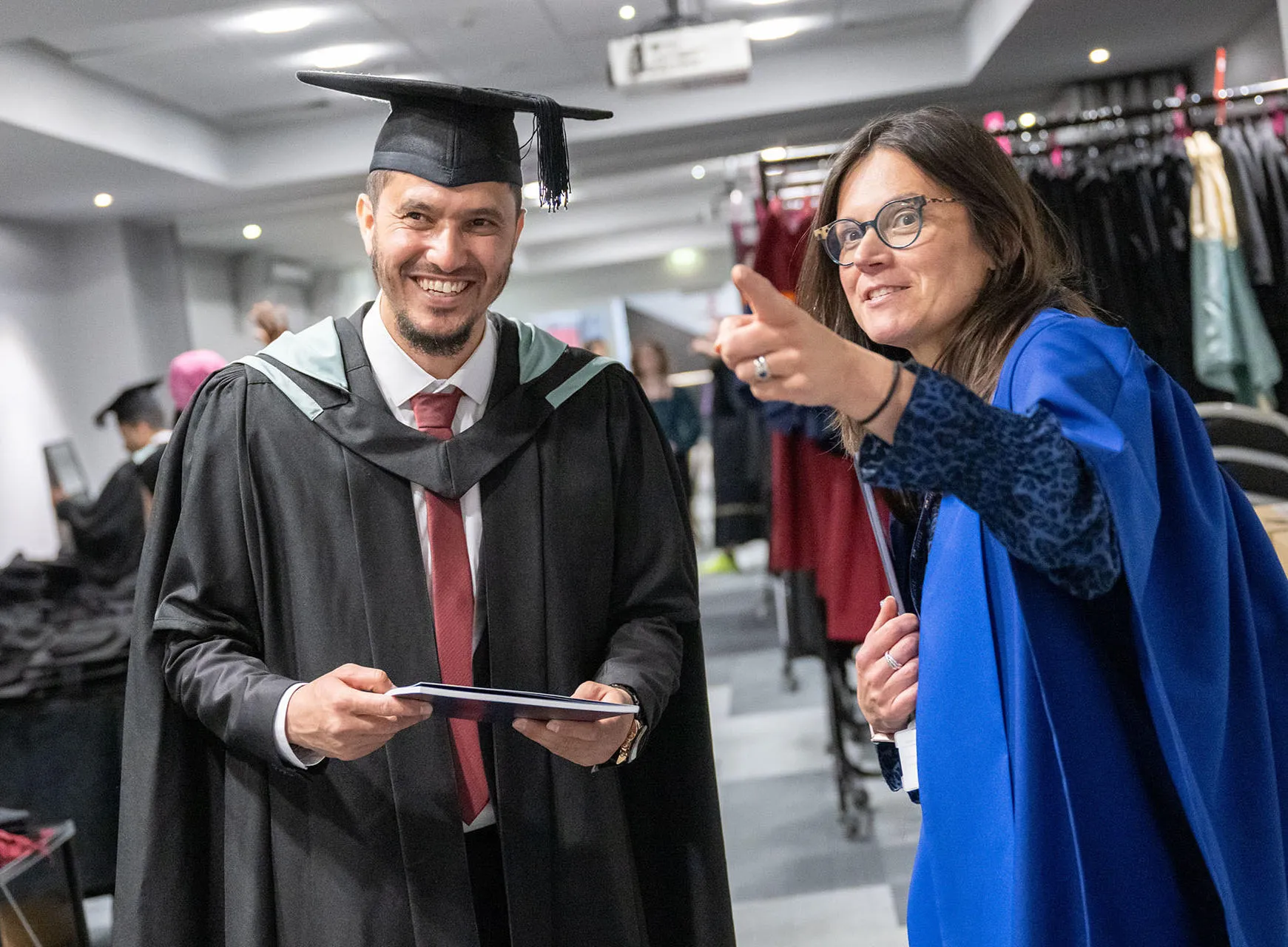Student holding graduation booklet and staff member pointing out directions