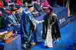 Student shaking hands with robed University chancellor on the graduation stage