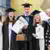 Three graduates celebrate with friends.