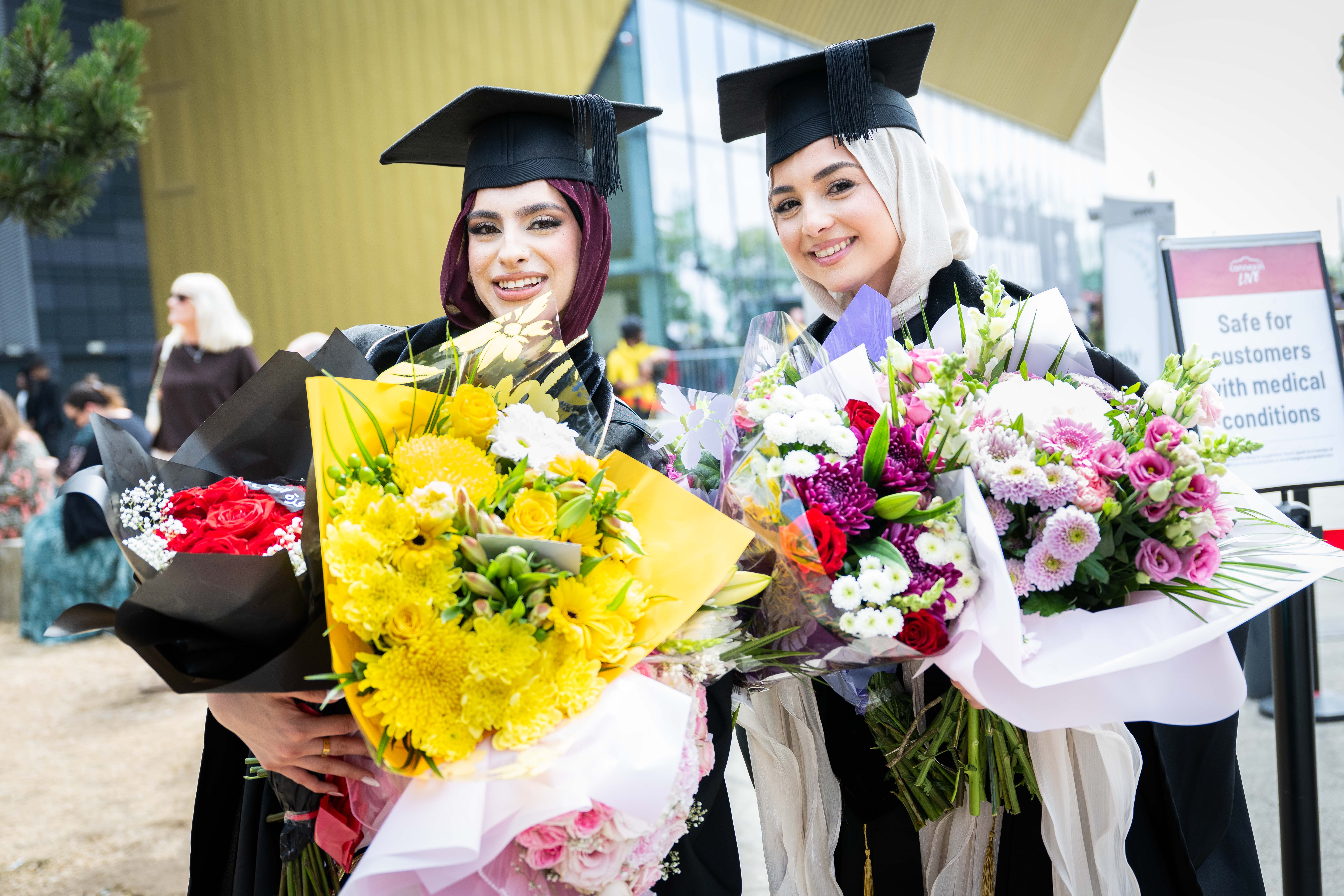 Graduates with bouquets of flowers. 