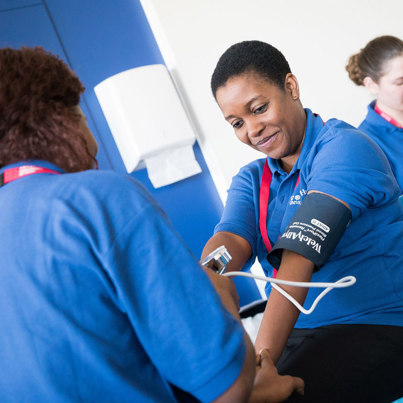 A woman sits having her blood pressure taken by another woman with her back to the camera