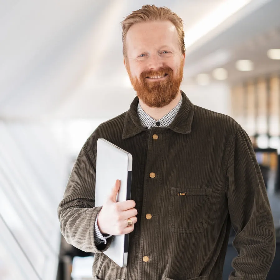 Smartly dressed man with a beard carrying a laptop in a brightly lit rom