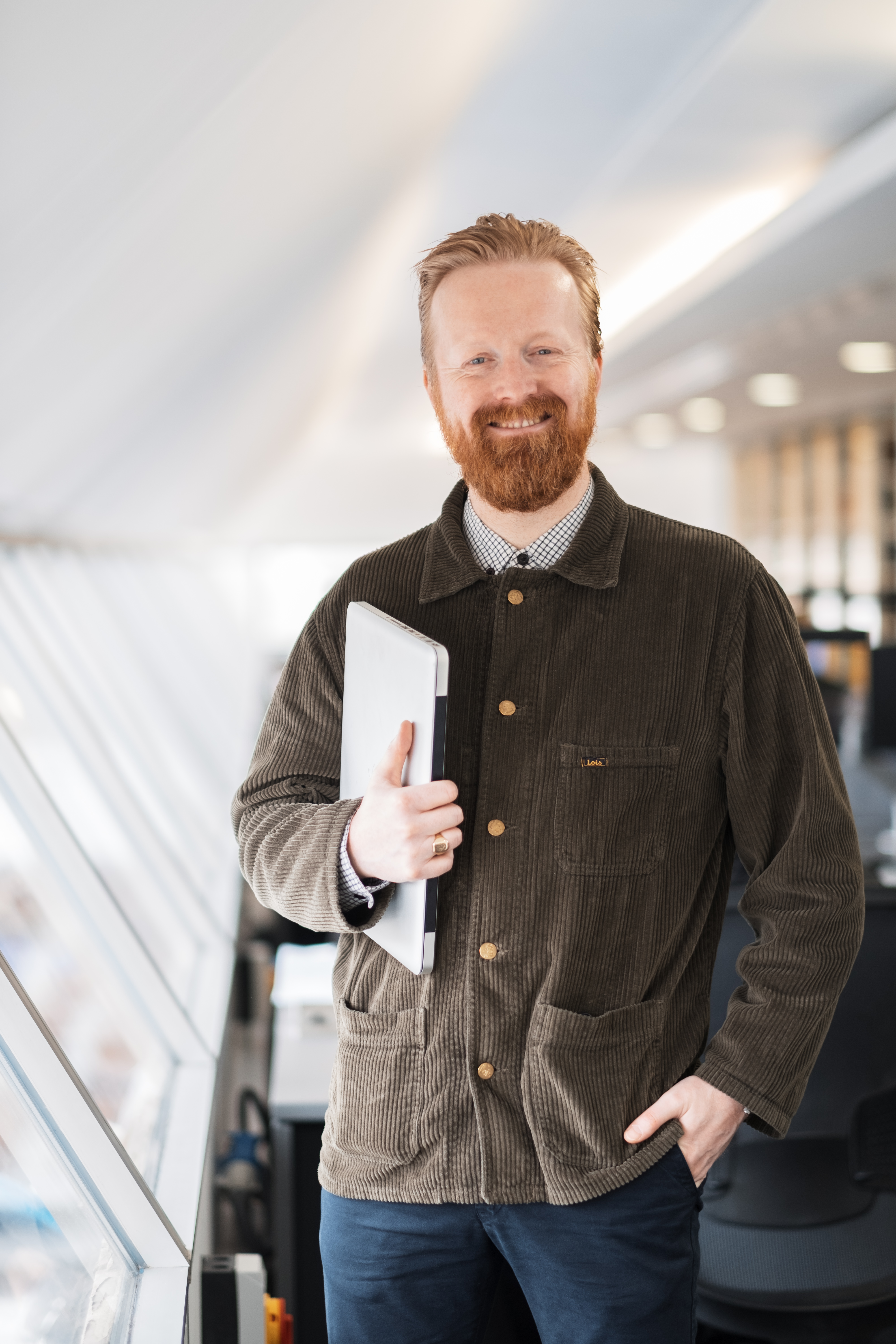 Smartly dressed man with a beard carrying a laptop in a brightly lit rom