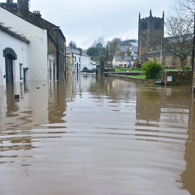 A flooded street with houses either side and a church in the background.