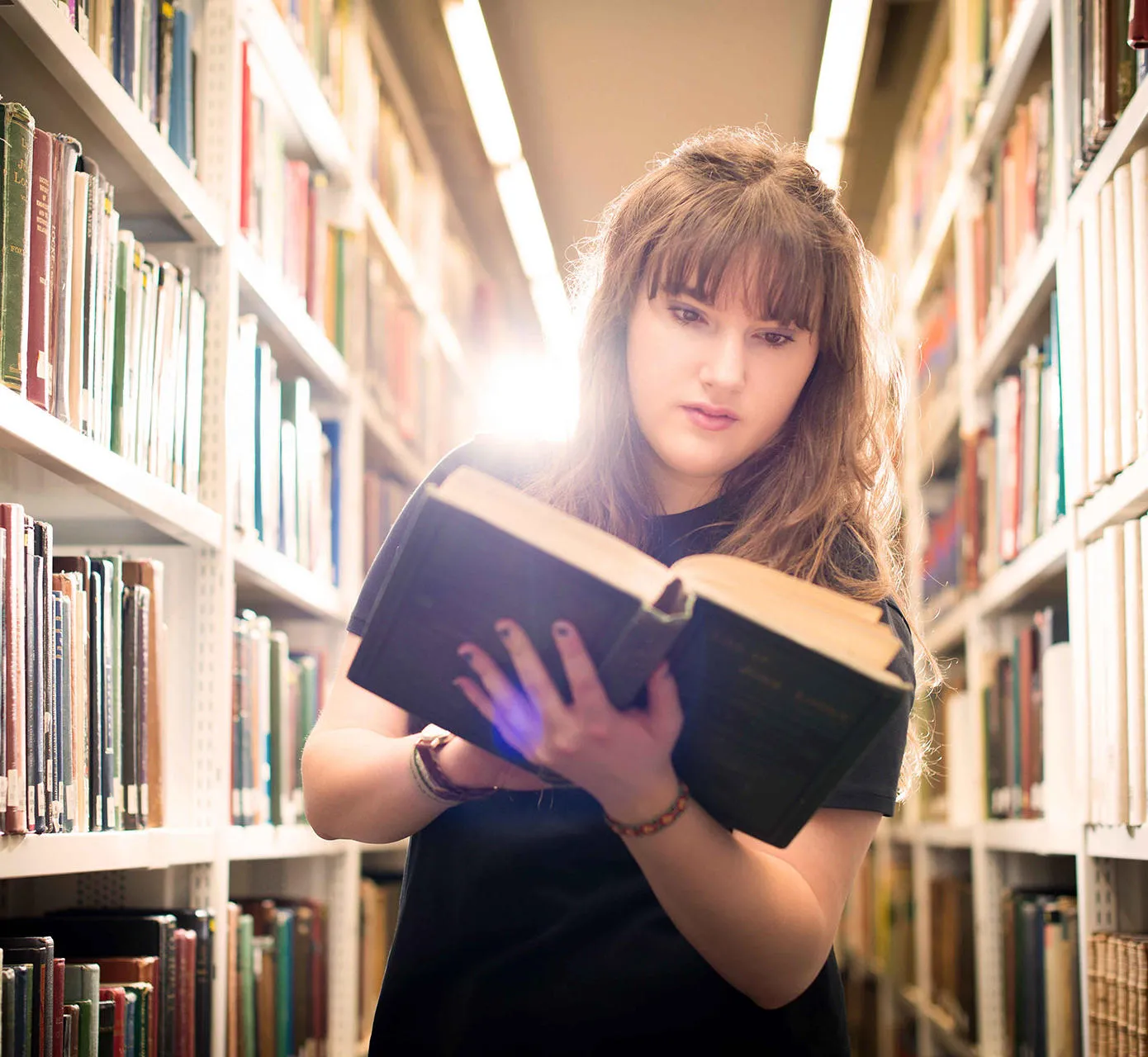 Student reading a book in library racks