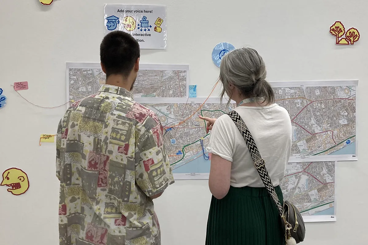 Two people discuss a display of illustrated maps 