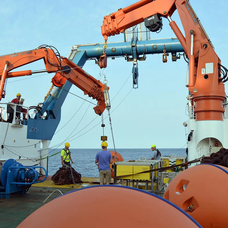 Scientists on a research vessel stand by two orange cranes