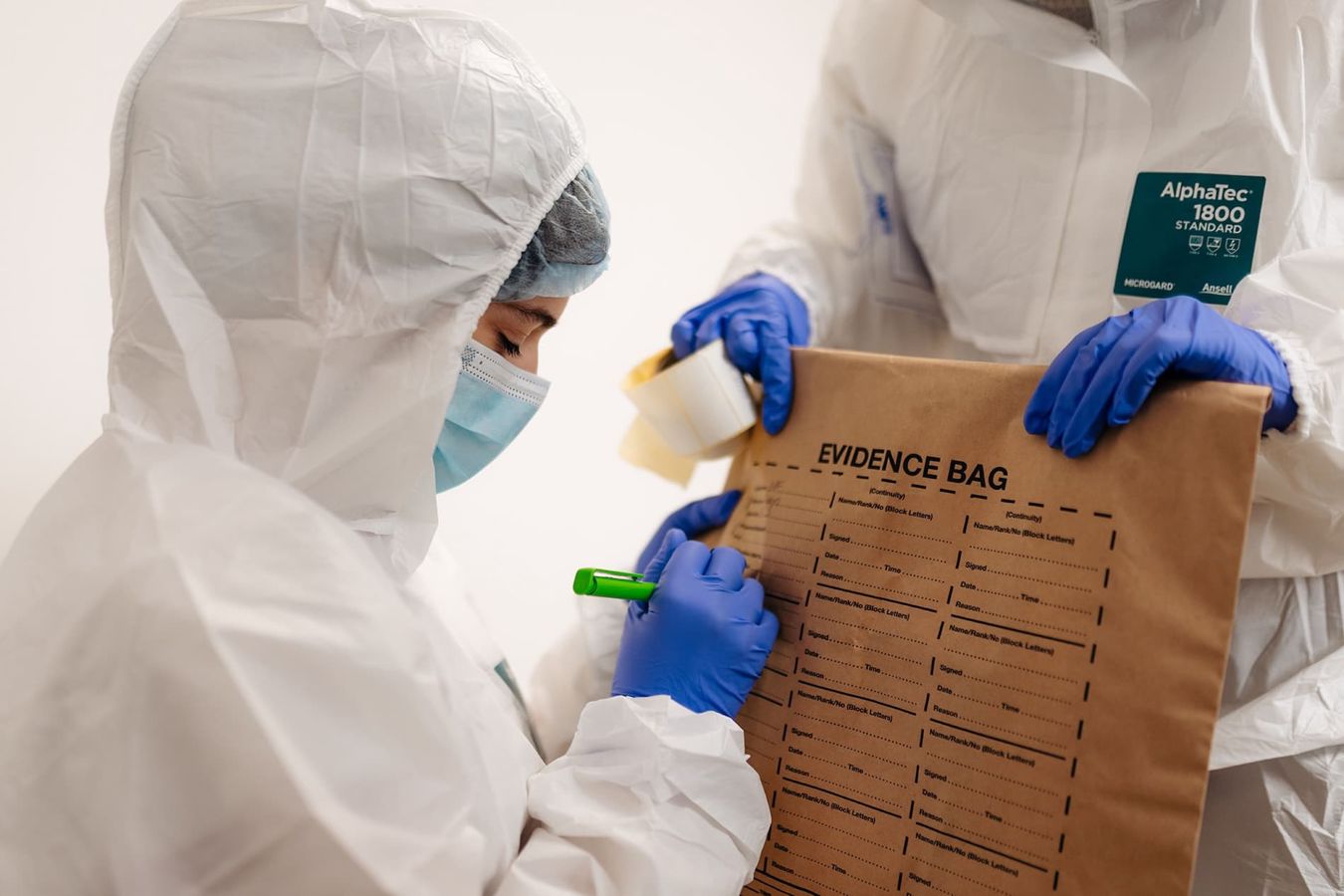 A student in white protective suit labels an evidence bag at a mock crime scene.