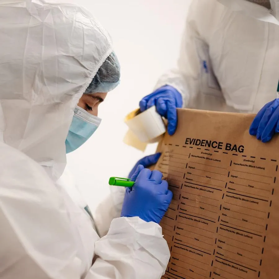 A student in white protective suit labels an evidence bag at a mock crime scene.