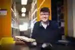 Student sits at a desk in a library with books and a laptop