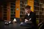 student studying on laptop with library shelving in the background