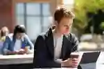 Student seated outdoors holding a coffee and looking at a tablet